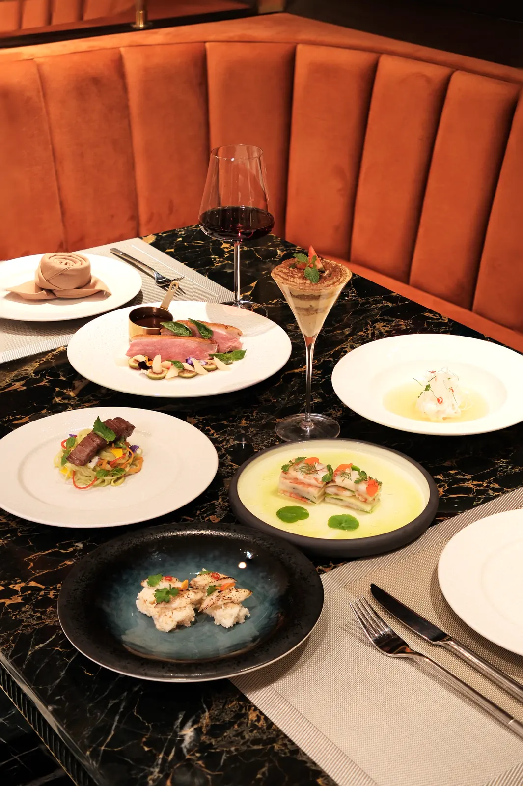 Table of several plated dishes and a glass of red wine — Lumé Restaurant · Classyc Hàng Buồm